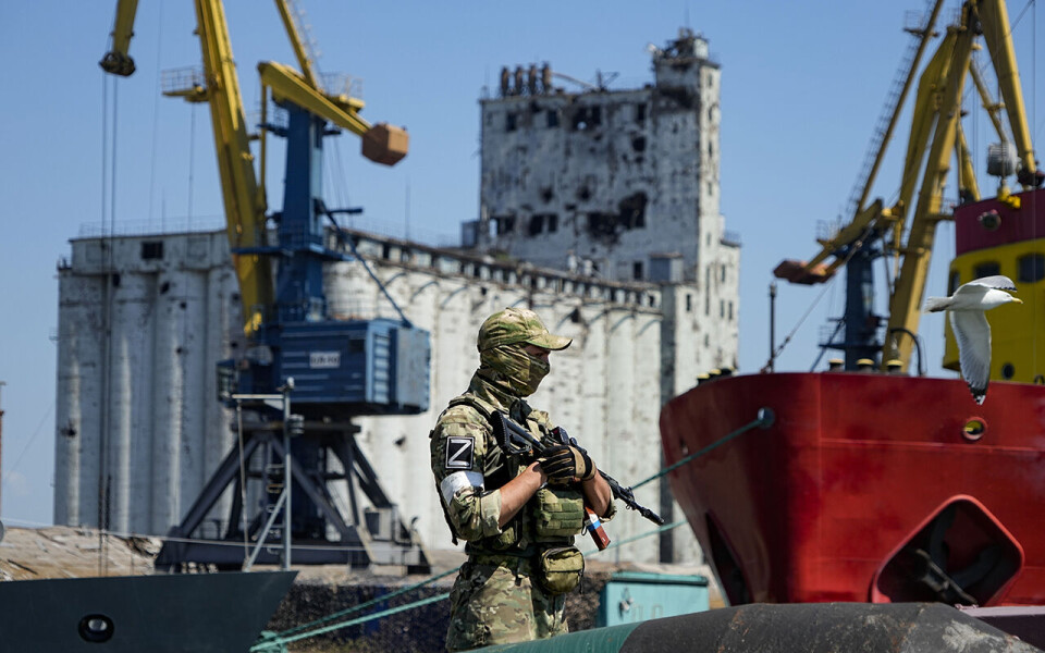 Foto En russisk soldat står vakt ved havnen i Mariupol, som nå er under russisk kontroll. Bygget i bakgrunnen er et kornlager. Russiske blokader av havnene i Ukraina gjør det umulig å eksportere korn fra landet. Arkivfoto: AP / NTB