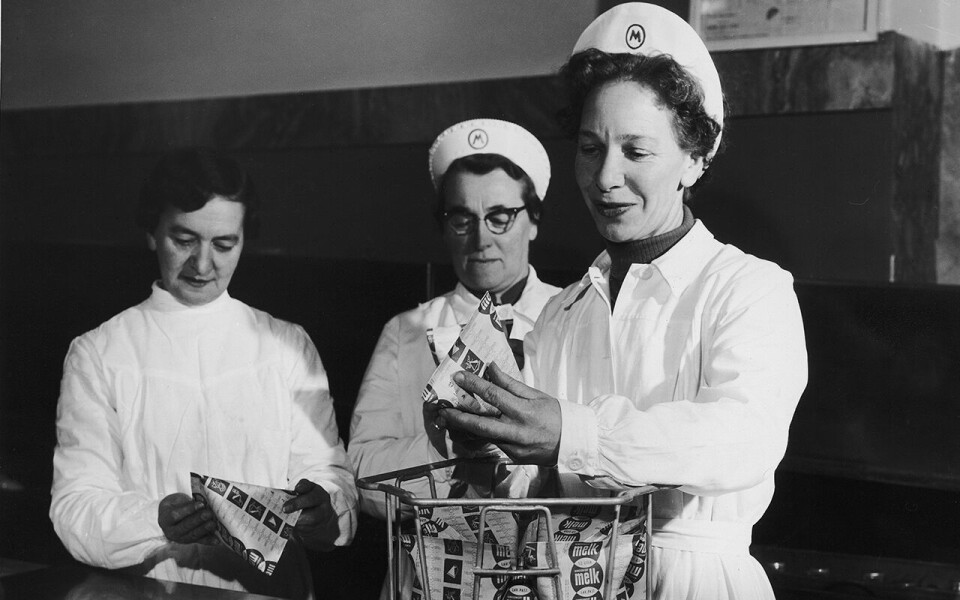 «Første dagen falt det vanskelig både for meieripersonalet og husmødrene å stable den nye kartongen slik at de tok minst mulig plass. Til høyre: Meieriansatt fru Ingeborg Engebretsen.»